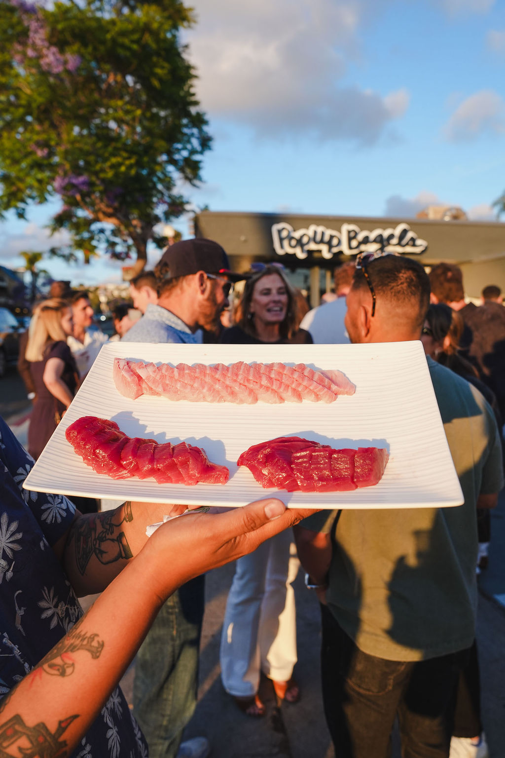 A sashimi platter passed through a sunset crowd